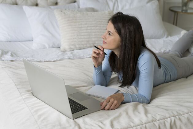 房子躺在床上用笔记本电脑打视频电话的女人通讯虚拟女性