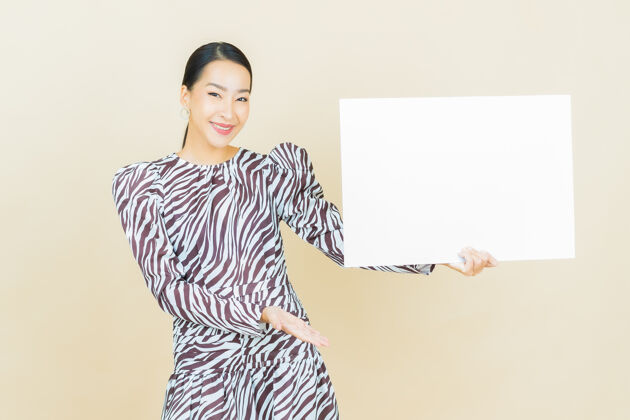 中国人肖像美丽的年轻亚洲妇女与空白的白色广告牌米色表亚洲人成人