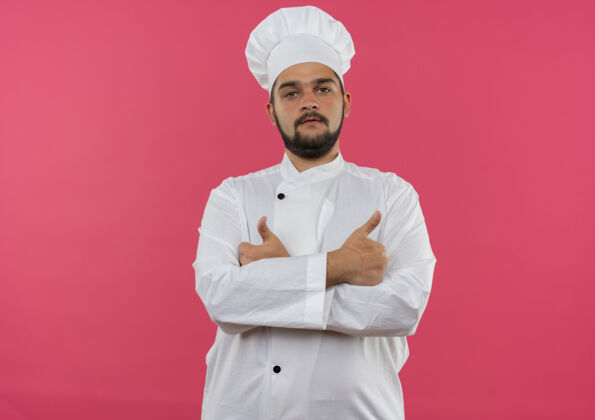 自信自信的年轻男性厨师身着厨师制服 以封闭的姿势站在粉色墙壁上 有复制空间封闭烹饪站立