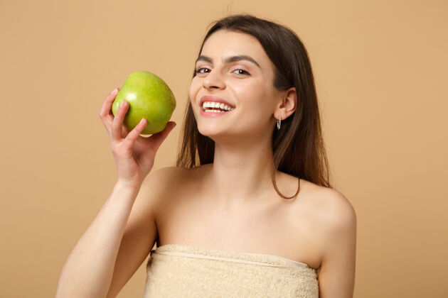护理特写黑发半裸完美皮肤的女人 裸妆把苹果隔离在米色粉彩墙上健身身体护理美容