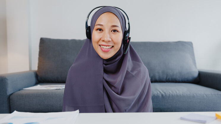 视频通话亚洲女士戴着耳机用笔记本电脑在客厅远程工作时 在视频电话会议上和同事谈论计划亚洲人印度人通信