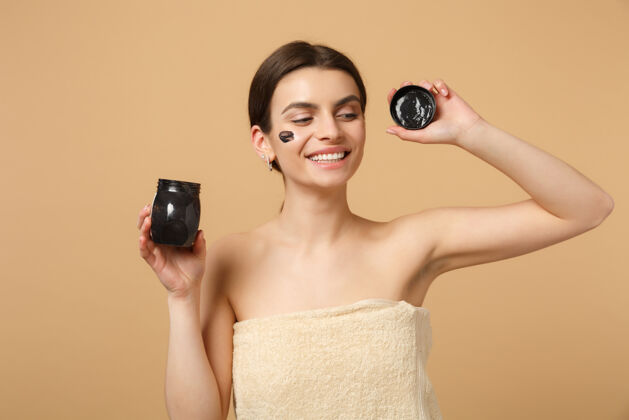 容器特写黑发半裸完美皮肤的女人 裸妆黑色面膜隔离在米色粉彩墙上身体治疗光滑