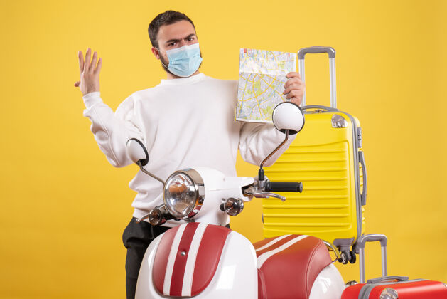 地图旅行概念的俯视图 戴着医用面罩的神经兮兮的家伙站在摩托车旁边 黄色手提箱在上面 手里拿着地图人医疗摩托车