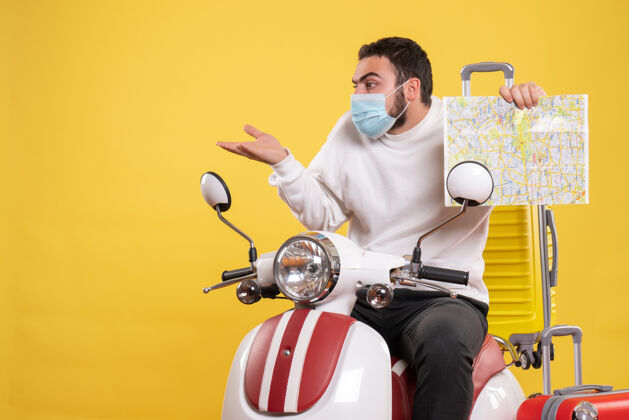 人旅行的概念与惊讶的家伙在医疗面具坐在摩托车上与黄色手提箱上 并显示黄色地图摩托车微笑摩托车