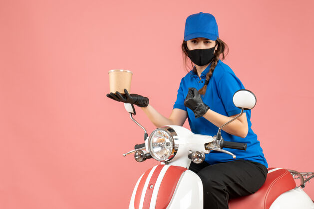 滑板车顶视图自信的女快递员戴着医用面罩和手套坐在滑板车上 在柔和的桃色背景下传递订单男人头盔