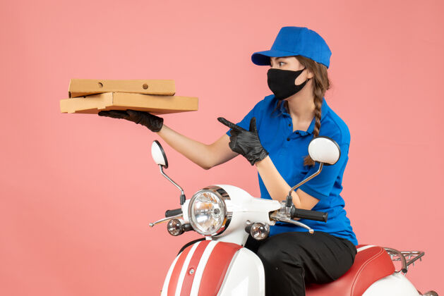 面具俯视图：年轻困惑的女快递员戴着医用口罩和手套坐在滑板车上用粉彩桃子送订单车辆年轻人
