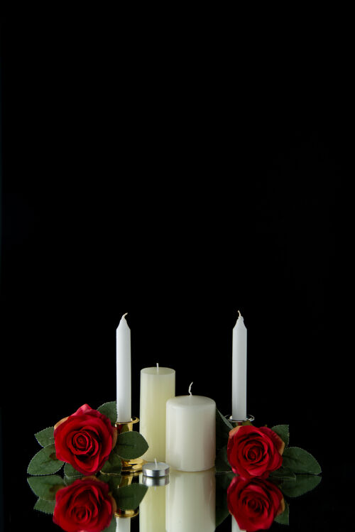 前面黑色墙壁上有红花的白色蜡烛的正视图白蜡烛火焰蜡烛