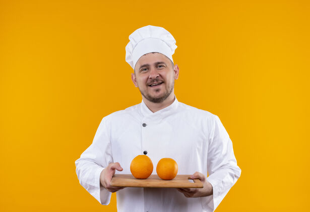 烹饪身着厨师制服的年轻帅哥 手里拿着一块插着橘子的砧板 孤零零地贴在橘子墙上董事会削减英俊