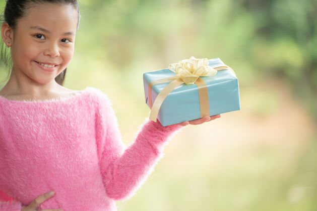 礼物圣诞快乐微笑的小女孩与礼品盒的肖像画在一棵绿色的树枝旁绿色的树叶从自然森林的背景中突出季节自然盒子