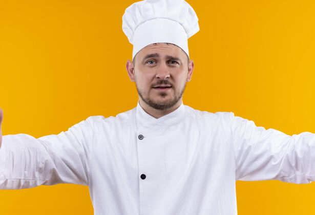 年轻自信的年轻帅哥厨师身着厨师制服站在孤零零的橙色墙上自信厨师帅气