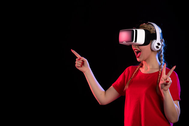 护目镜戴着耳机在黑暗的墙上玩虚拟现实的年轻女士的正视图游戏黑暗肖像