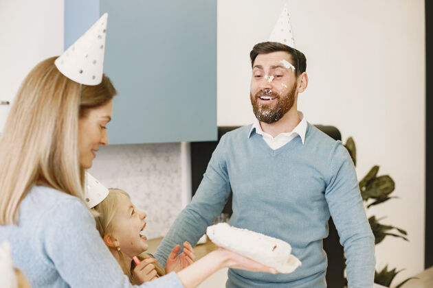 爸爸妈妈和女儿在厨房庆祝爸爸生日妈妈在男人脸上打蛋糕漂亮吹自制