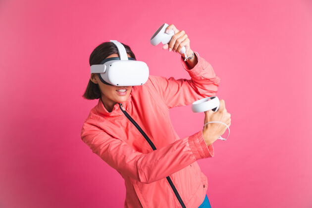 科技穿着运动夹克 戴着虚拟现实眼镜的年轻健美女士在粉红色的舞台上玩拳击比赛科技虚拟现实耳机享受