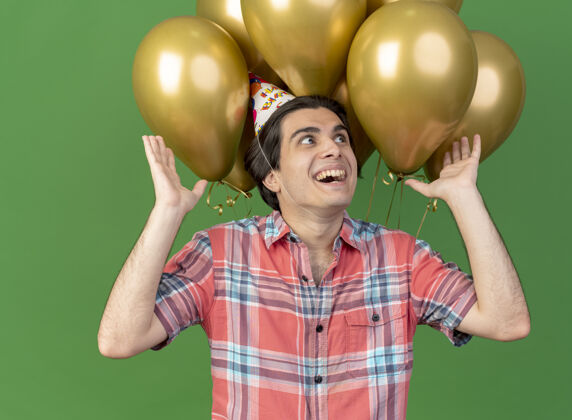 气球戴着生日帽的高加索帅哥兴奋地举起双手站在氦气球前正面手绿色