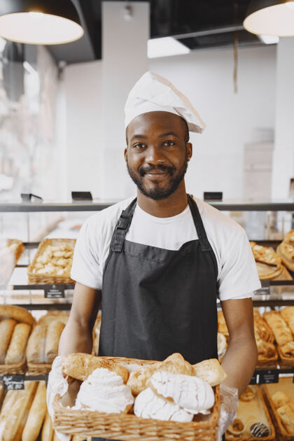 服务非洲裔美国面包师和新鲜面包在面包店的肖像糕点厨师拿着小糕点厨师自信表情