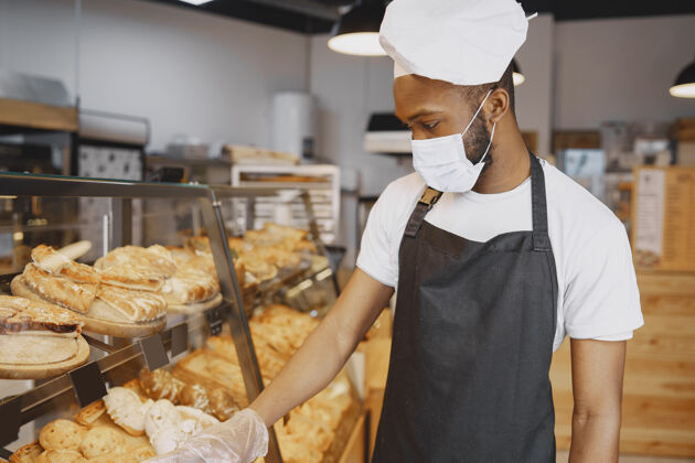 忙碌穿制服的面包师给糕点的建议戴防护面具的人买新鲜的面包男人骄傲自信