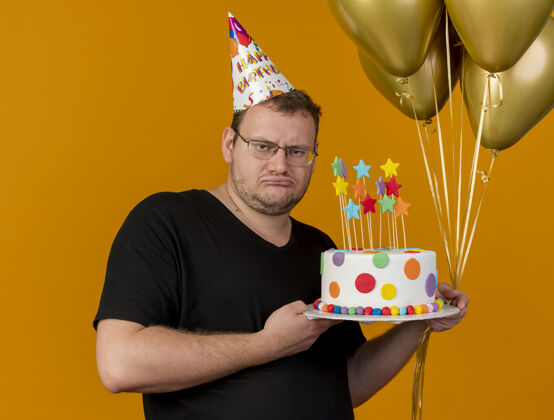 生日心烦意乱的成年斯拉夫人戴着眼镜 戴着生日帽 手里拿着氦气球和生日蛋糕空间成人气球