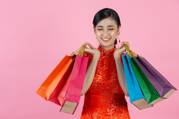 女人美丽的亚洲女人快乐的微笑和购物在中国新年的粉红色背景新购物展示
