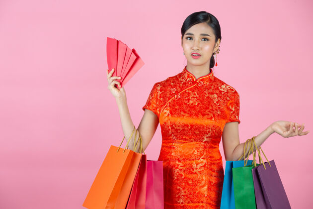 女性美丽的亚洲女人快乐的微笑和购物在中国新年的粉红色背景年空白手势