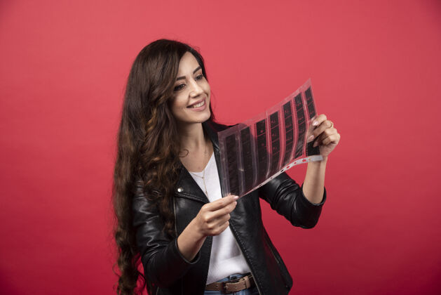 镜头一个年轻的女人在看一个红色背景的带照片的文件高质量的照片年轻磁带拿着