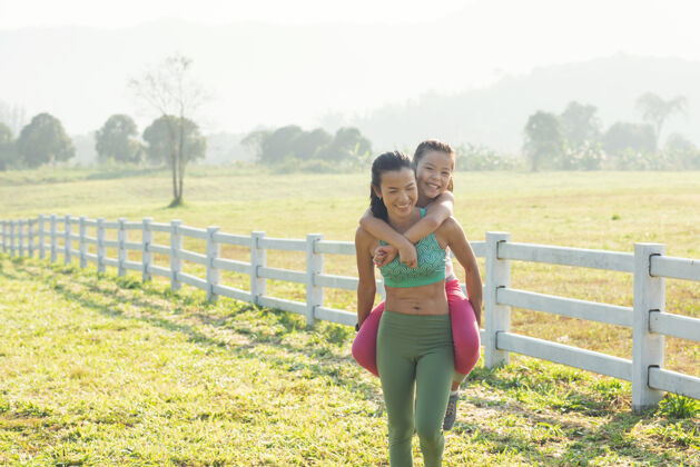孩子可爱的小女儿和妈妈一起骑在背驮上 在乡下度过了一段时间在大自然里 夏天的草地上有一个幸福的家庭户外运动与健身 运动学习促进儿童发展锻炼慢跑家庭