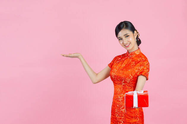 东方美丽的亚洲女人开心的微笑 拿着粉红色背景的中国新年礼盒微笑展示人