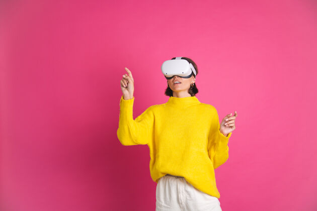 虚拟美丽的女人穿着亮黄色的毛衣 戴着粉色的虚拟现实眼镜 开心地用手指指着左边的空白处界面女性头发