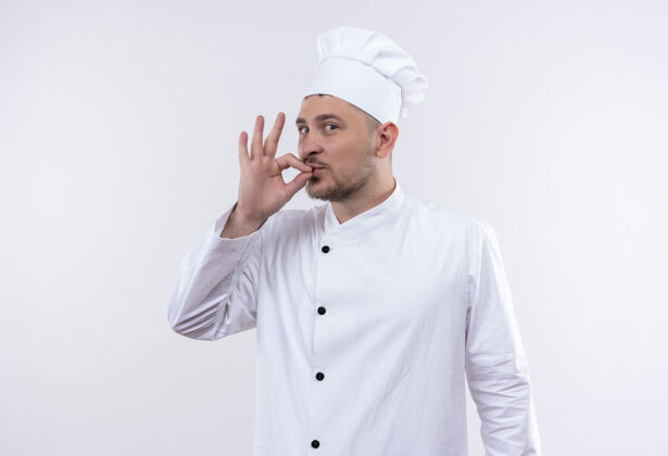 年轻印象深刻的年轻帅哥厨师在厨师制服做美味的标志隔离在白色的墙壁上制服美味帅气
