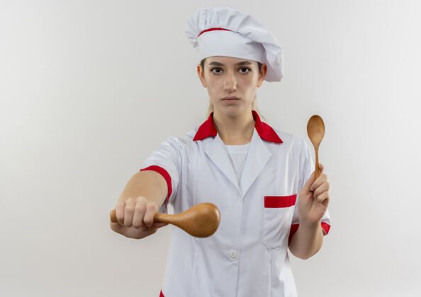 勺子自信的年轻漂亮厨师穿着厨师制服 拿着勺子 伸出勺子 孤立地站在白色的墙上拿着伸展自信