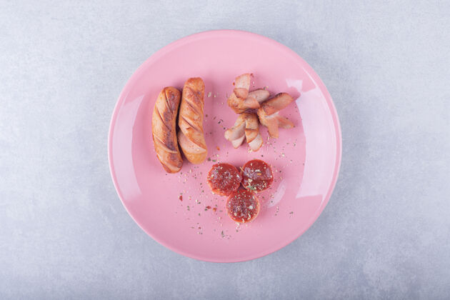 烤各种形状的炒香肠放在粉红色的盘子里美味辛辣美味