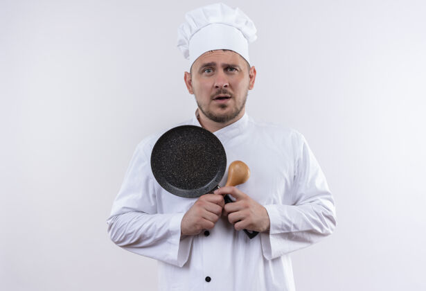 厨师年轻帅气的厨师穿着厨师制服 拿着勺子和煎锅站在隔离的白色墙上印象薯条制服