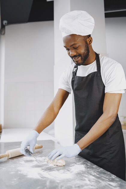 货架非裔美国面包师在烘焙生产中为糕点准备生面团为糕点捏面团面团帽子粉末