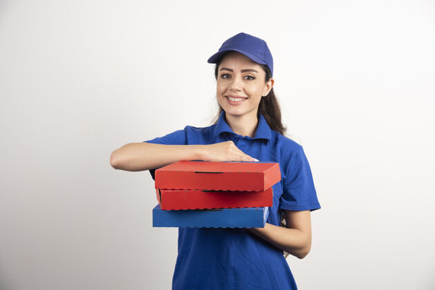 快递员身着蓝色制服的快乐微笑送货女孩 白色背景上有外卖披萨盒高质量照片食品工作年轻人