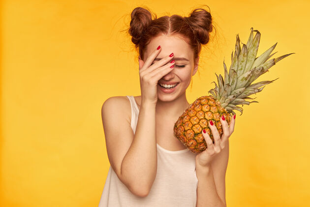 肖像一个漂亮的红发女孩的画像 有两个发髻手举在脸上 感到害羞穿着白衬衫 手里拿着菠萝完美果汁漂亮