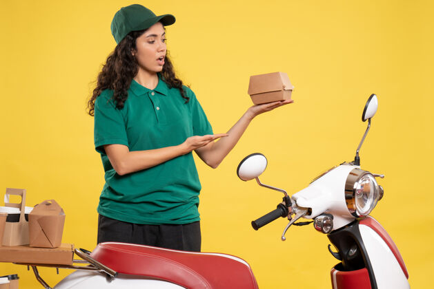 食物正面图：身着绿色制服的女快递员 黄色背景上有一个小食品包 工作颜色为工作递送食品的女服务人员工作球员高尔夫球手