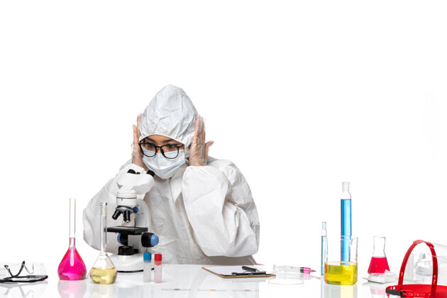 盖子正面图身着特殊防护服的年轻女化学家在白色办公桌上用显微镜工作病毒-化学实验室套装实验室外套外套