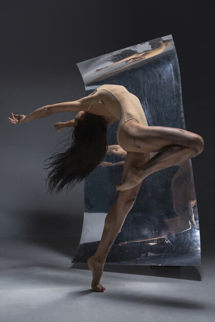 动作年轻时尚的现代芭蕾舞演员在灰色的墙壁上 镜子和幻觉反射在表面优雅女性动作