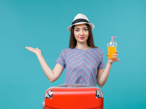 成人前视图：度假中的女人拿着她的红色袋子 在蓝色背景上拿着她的果汁旅行度假女人旅行旅行包果汁