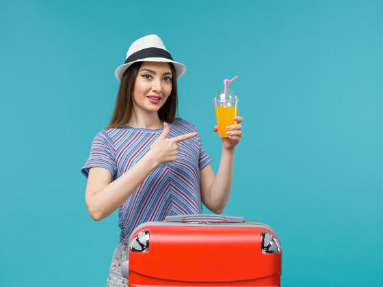 微笑正面图：度假中的女人 红色的袋子里装着她的果汁 蓝色的背景 旅途 旅途 度假 女性旅行旅行包果汁