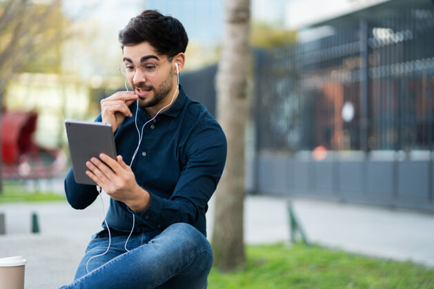 视频通话年轻人坐在户外的长椅上通过数码平板电脑进行视频通话的照片城市概念通话使用男人