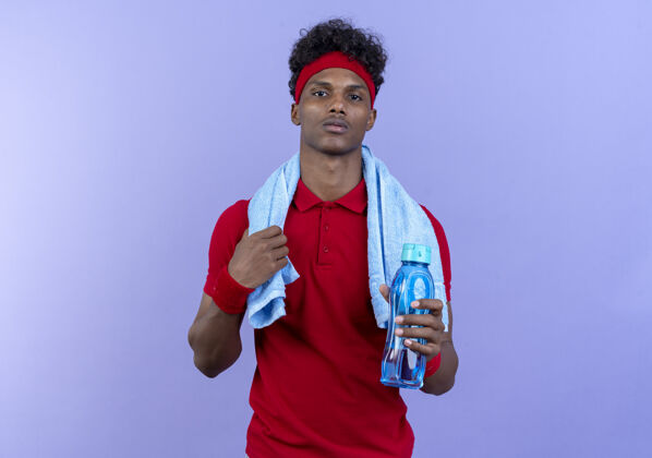 瓶子自信的年轻美国黑人运动男子戴着头带和腕带拿着水瓶和毛巾在肩上穿男人腕带