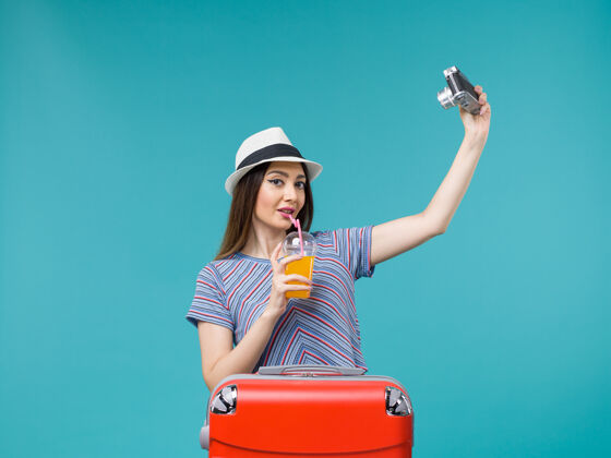 举行正面图：度假中的女人拿着果汁 用相机拍摄蓝色背景的航行 夏季旅行 海上旅行成人果汁航行