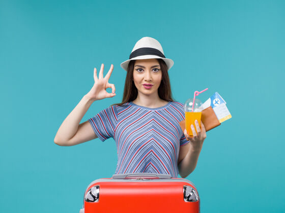 持有前视图度假妇女与她的红色袋子举行了蓝色背景旅行度假女性票和果汁旅行女微笑