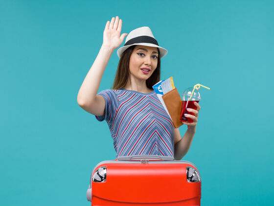 果汁前景度假中的女人拿着果汁和机票上蓝色背景的航程女性海上避暑飞机成人票旅程