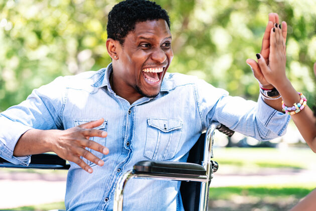 享受坐在轮椅上的非洲裔美国人和她的女儿在公园里玩得很开心男性快乐孩子