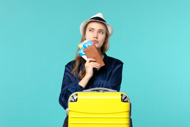 肖像正面图年轻女子拿着她的票准备旅行蓝色背景旅行飞机海上度假旅行的思考美丽年轻女子票