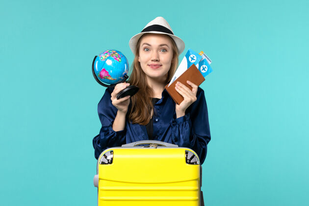 欢呼正面图年轻女子拿着机票和小地球仪在蓝色背景的飞机上海上度假旅行航程小微笑