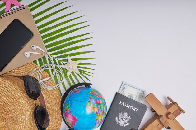 时尚白色背景上的平铺旅行配件 带棕榈叶 相机 帽子 护照 钱 地球仪 书 电话 地图和太阳镜顶视图 旅行或度假概念夏季背景金钱智能钱包