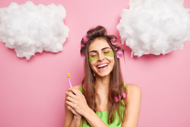 牙齿积极无忧无虑的女孩做完美的发型拿着牙刷去刷牙享受早晨的日常护理abot皮肤使用胶原蛋白垫微笑着牙齿隔离在粉红色的墙上云起来胶原蛋白早晨美丽