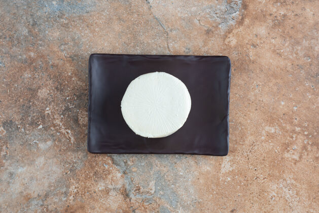 圆形大理石上黑色平板上白色圆形奶酪的俯视图白色美味盘子